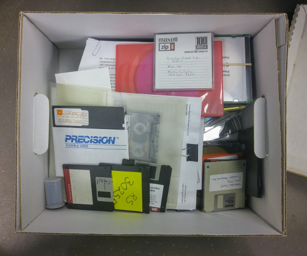 An archival box full of legacy media in the section author’s workspace, waiting to be transferred to stable formats.